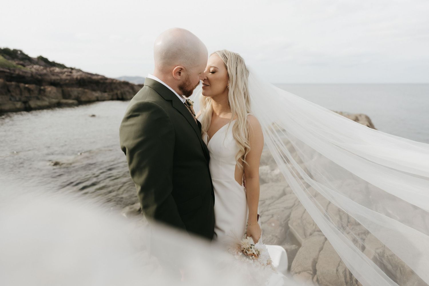 Elegant wedding couple shares a moment on rocky coastal cliffs overlooking the ocean.