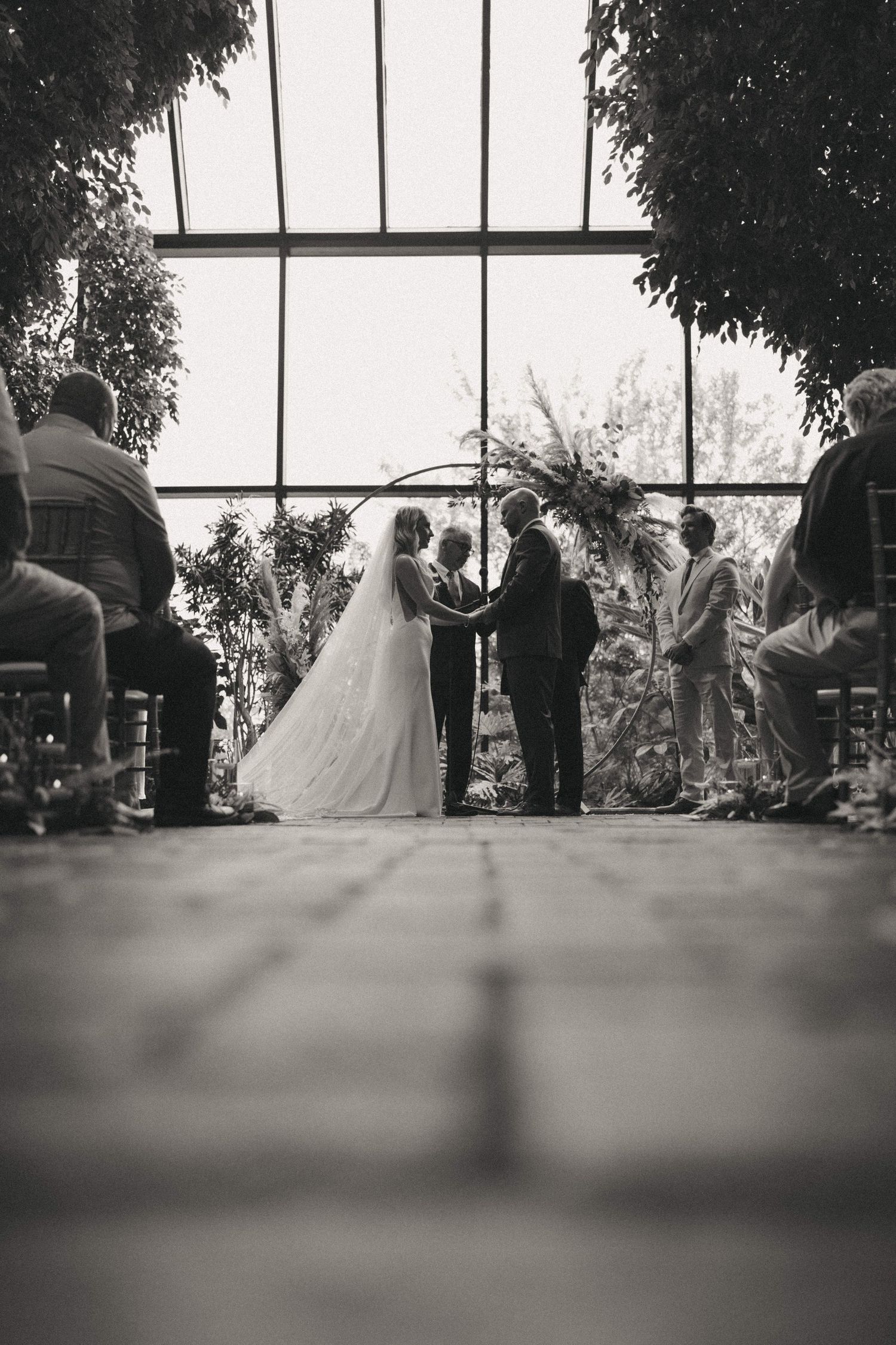 A black and white panoramic view of a wedding ceremony with guests seated indoors.