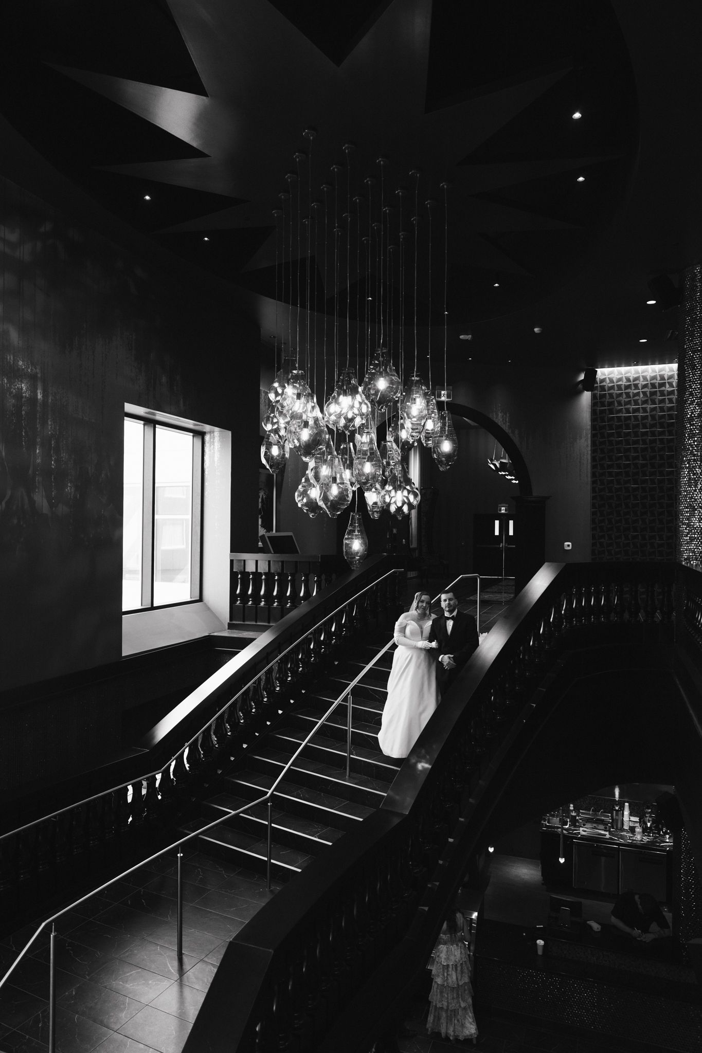 Dramatic black and white photo on grand staircase with hanging chandeliers.