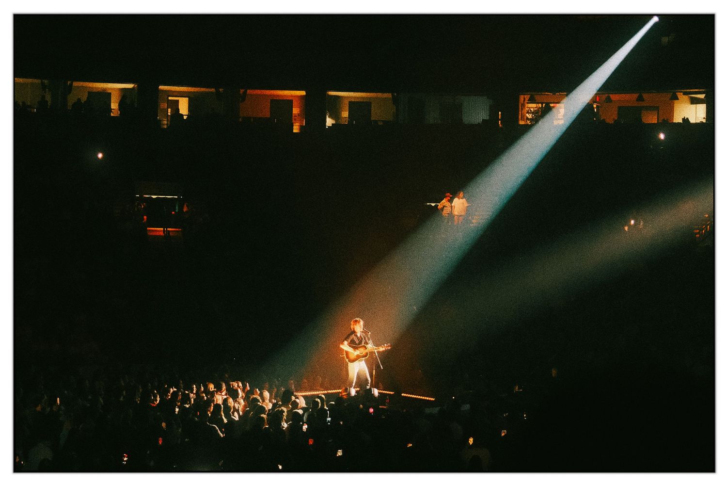 Dramatic concert performance on stage with bright spotlights illuminating the dark venue.