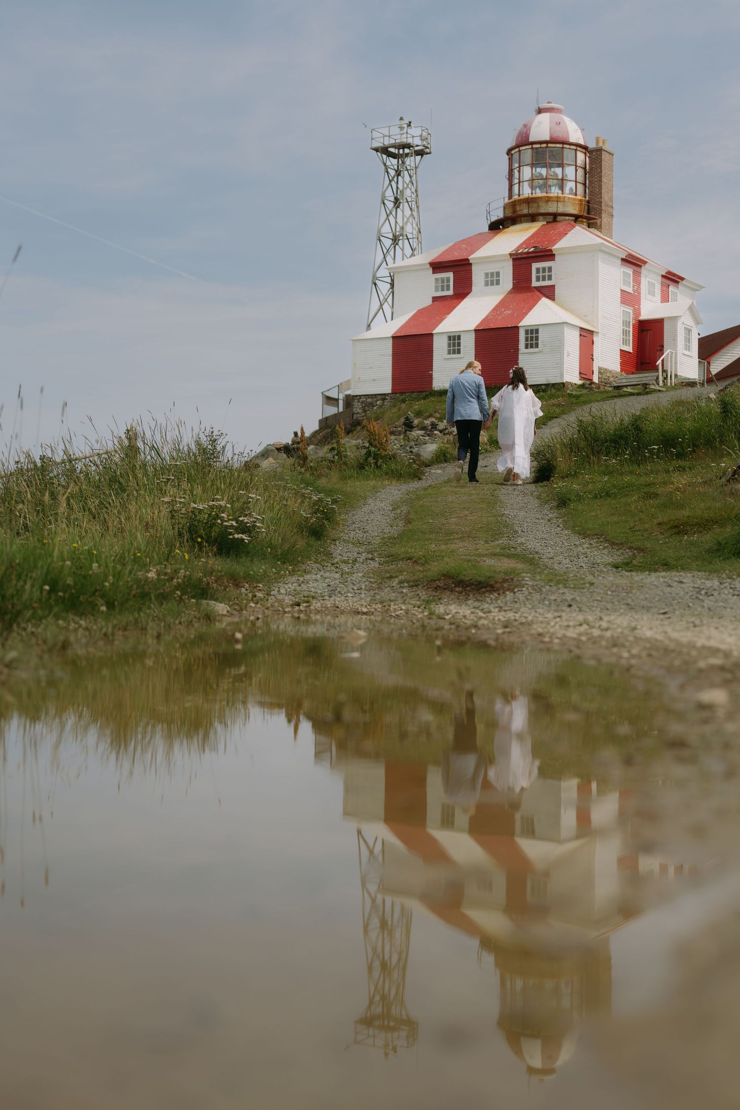 Red and white lighthouse reflected in calm water at Cape Bonavista in Newfoundland on an overcast day.