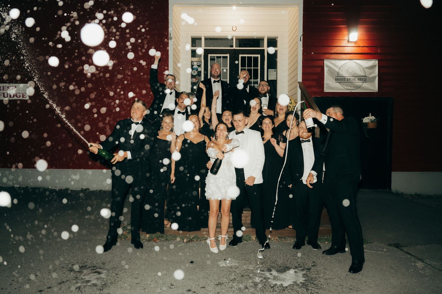 Wedding guests throw white flower petals at a nighttime celebration outside a venue.