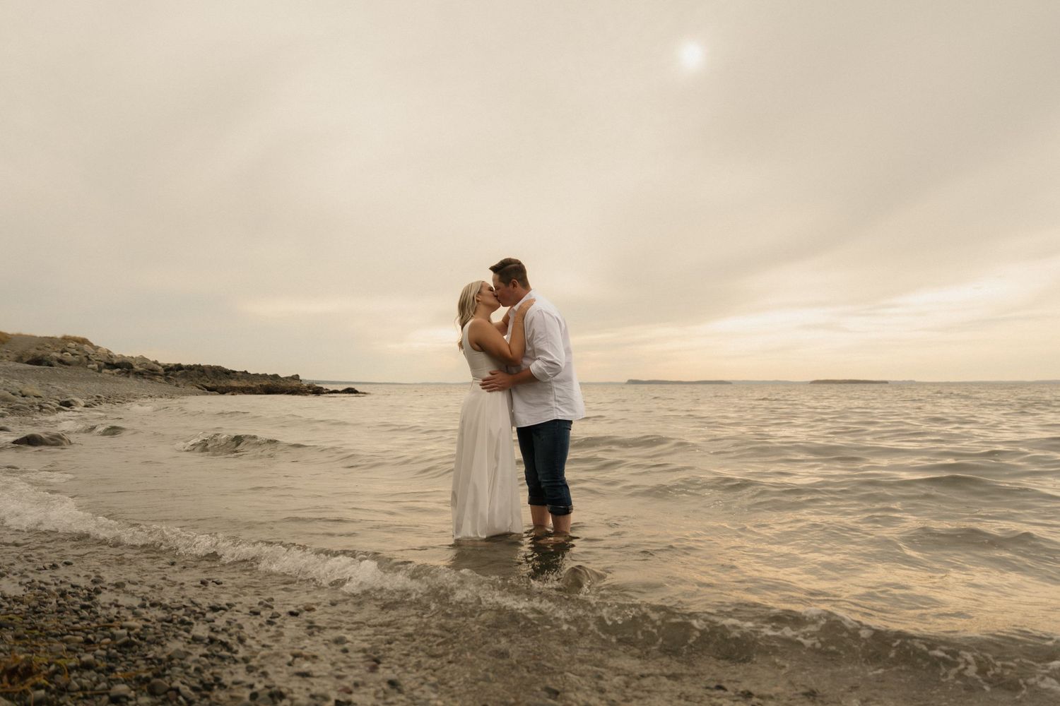 A romantic moment unfolds on a cloudy beach as waves crash against the shoreline at dusk.