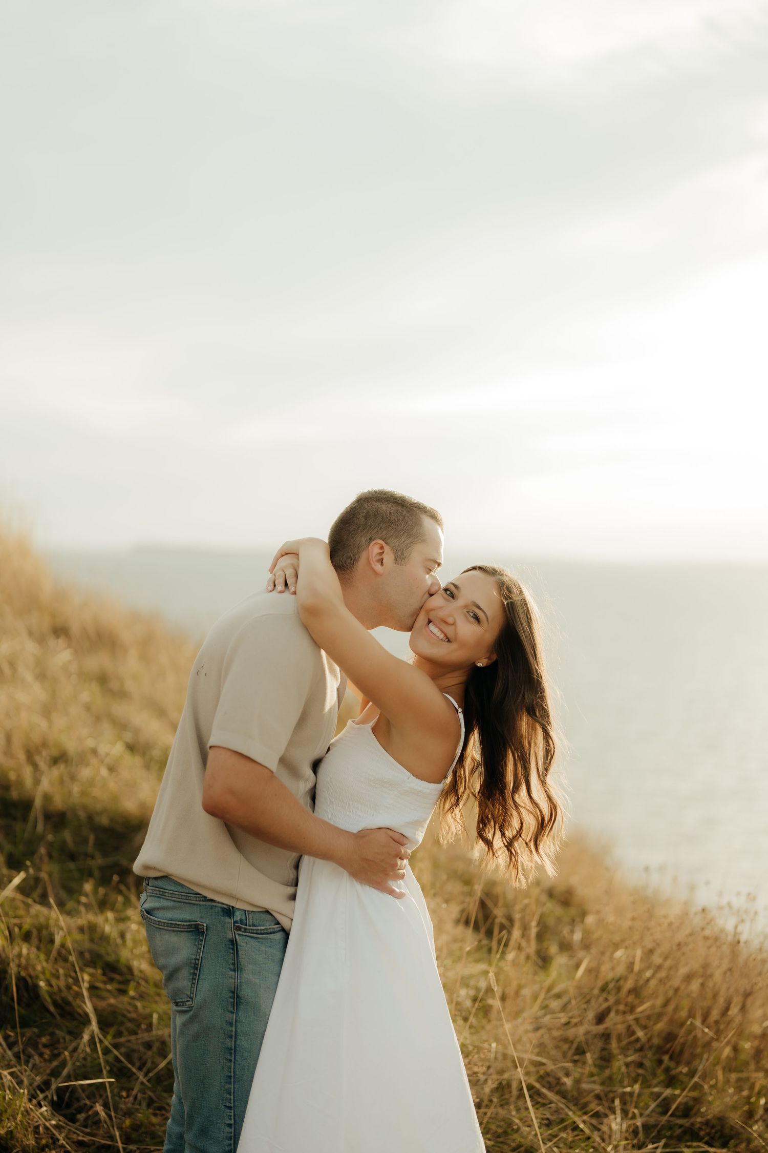 A romantic couple embraces in a golden field at sunset, creating a dreamy outdoor portrait.