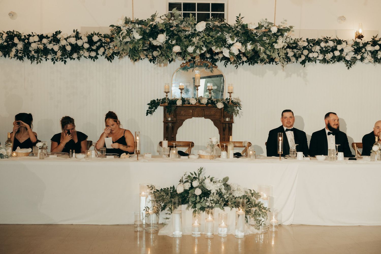 Wedding reception venue decorated with elegant greenery garlands and white floral arrangements along the walls.