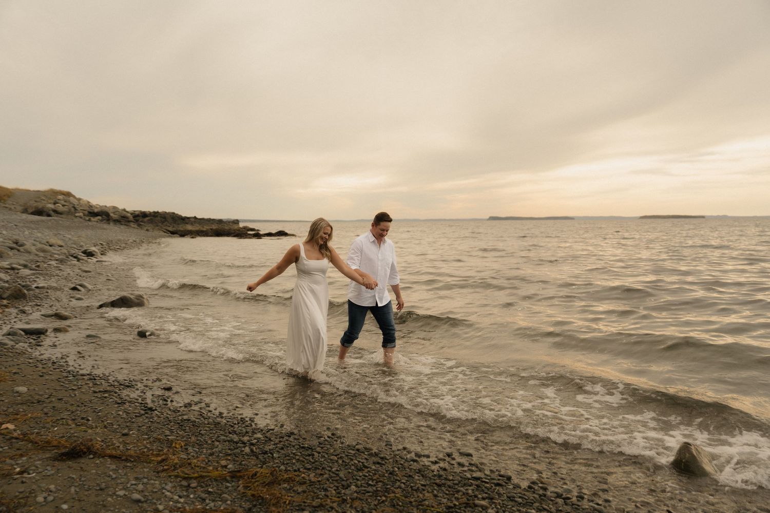 Couple splashing and playing in ocean waves during sunset beach session.