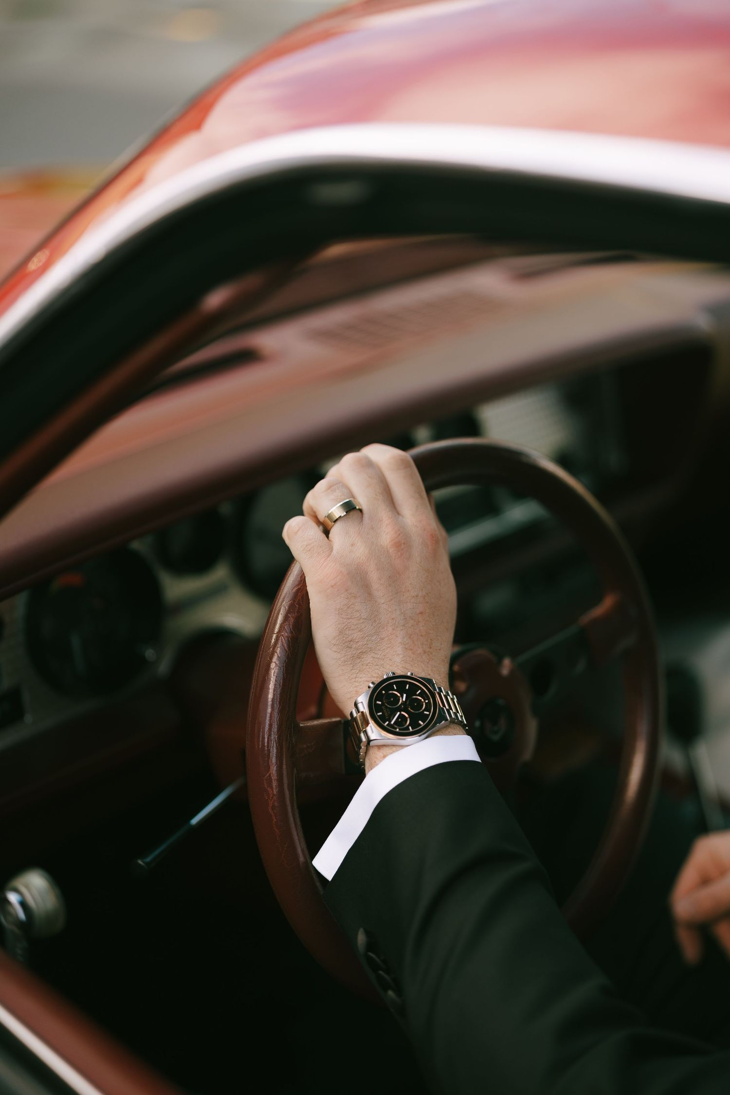 Man in suit wearing gold watch and ring grips vintage car steering wheel.