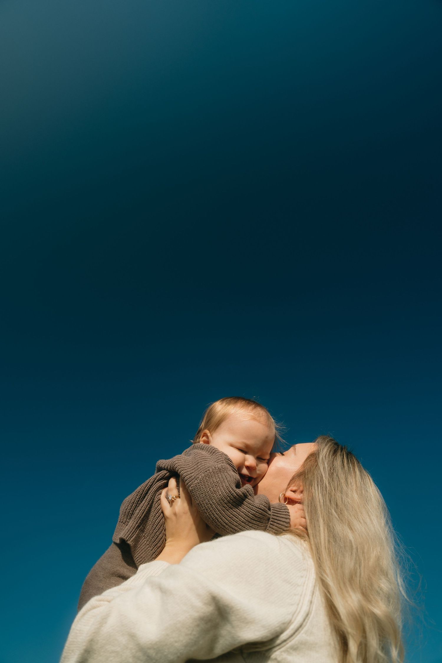 A couple in a romantic embrace kiss against a deep blue background while wearing cozy sweaters.