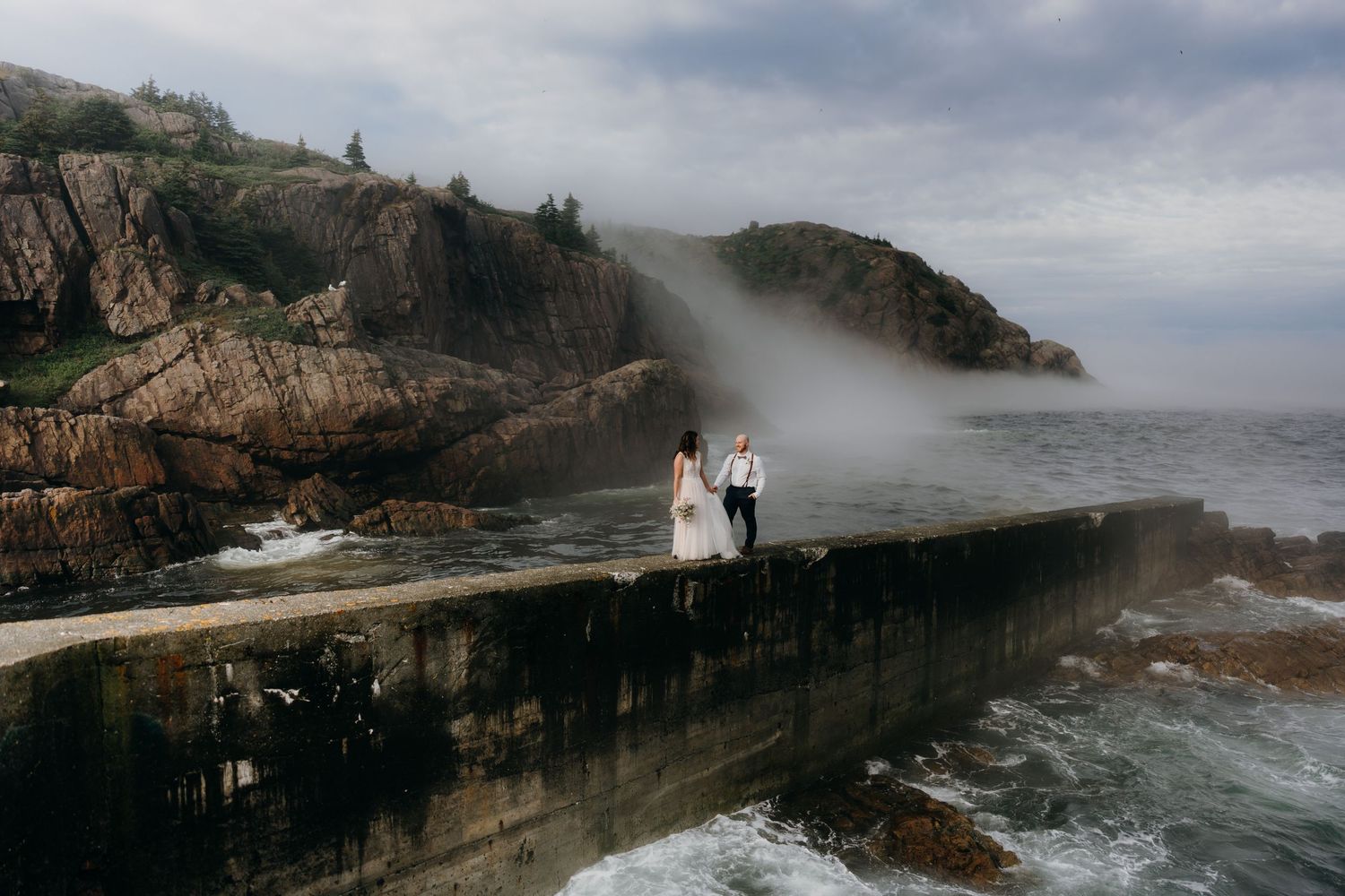 Dramatic coastal wedding photography sequence showing a couple on a rocky cliff as fog rolls in over the ocean.