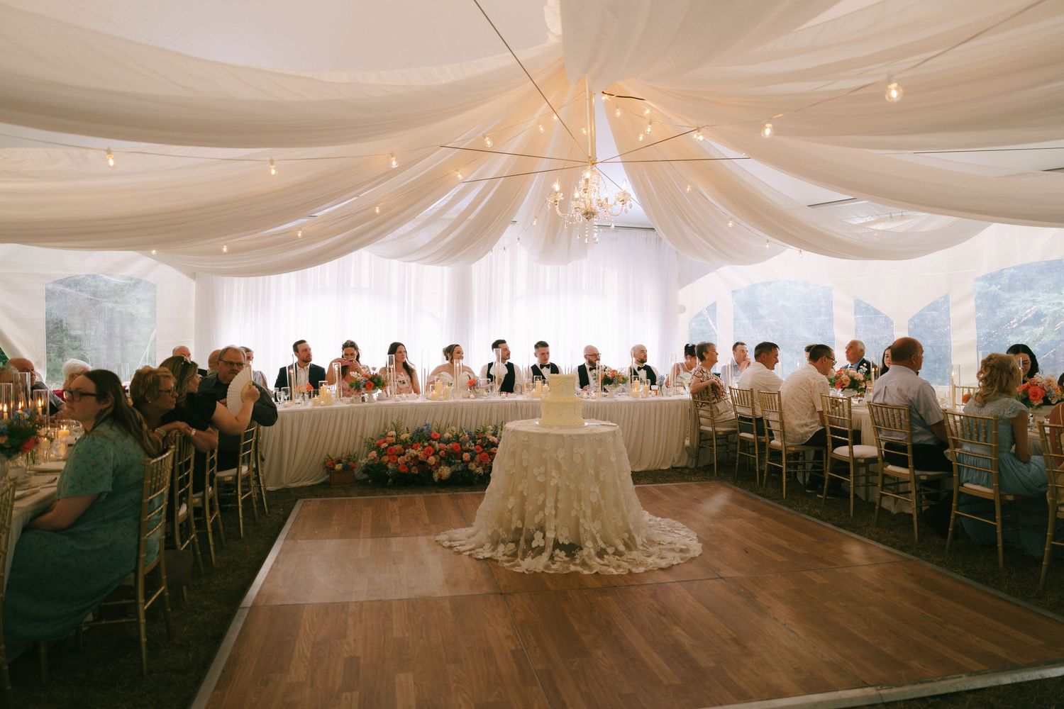A panoramic view of an elegant wedding reception tent with white draping and classic table settings.