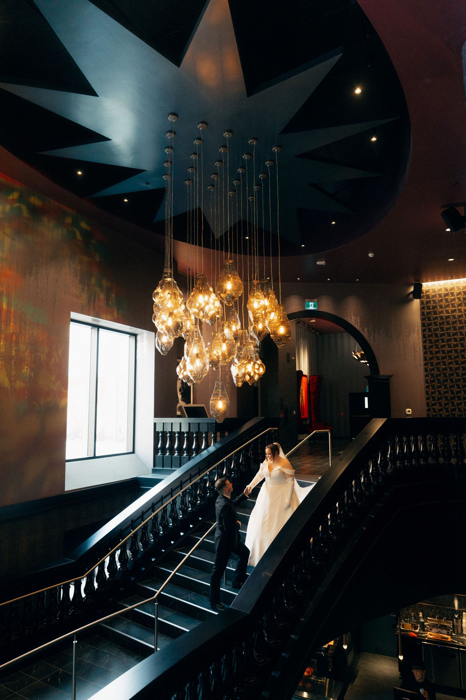 A dramatic wedding scene on a staircase with hanging crystal chandeliers and moody lighting creates an elegant atmosphere.