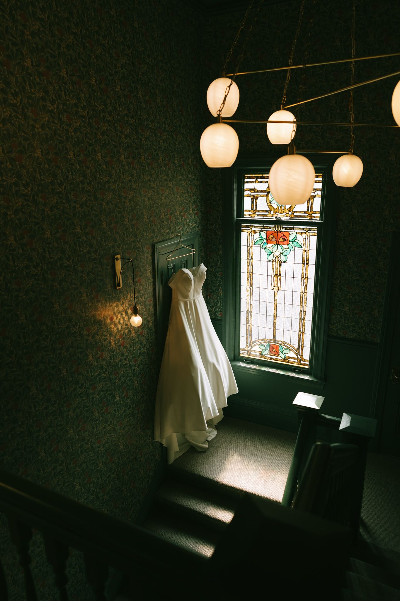 Wedding dress displayed near ornate stained glass window with glowing paper lanterns above.