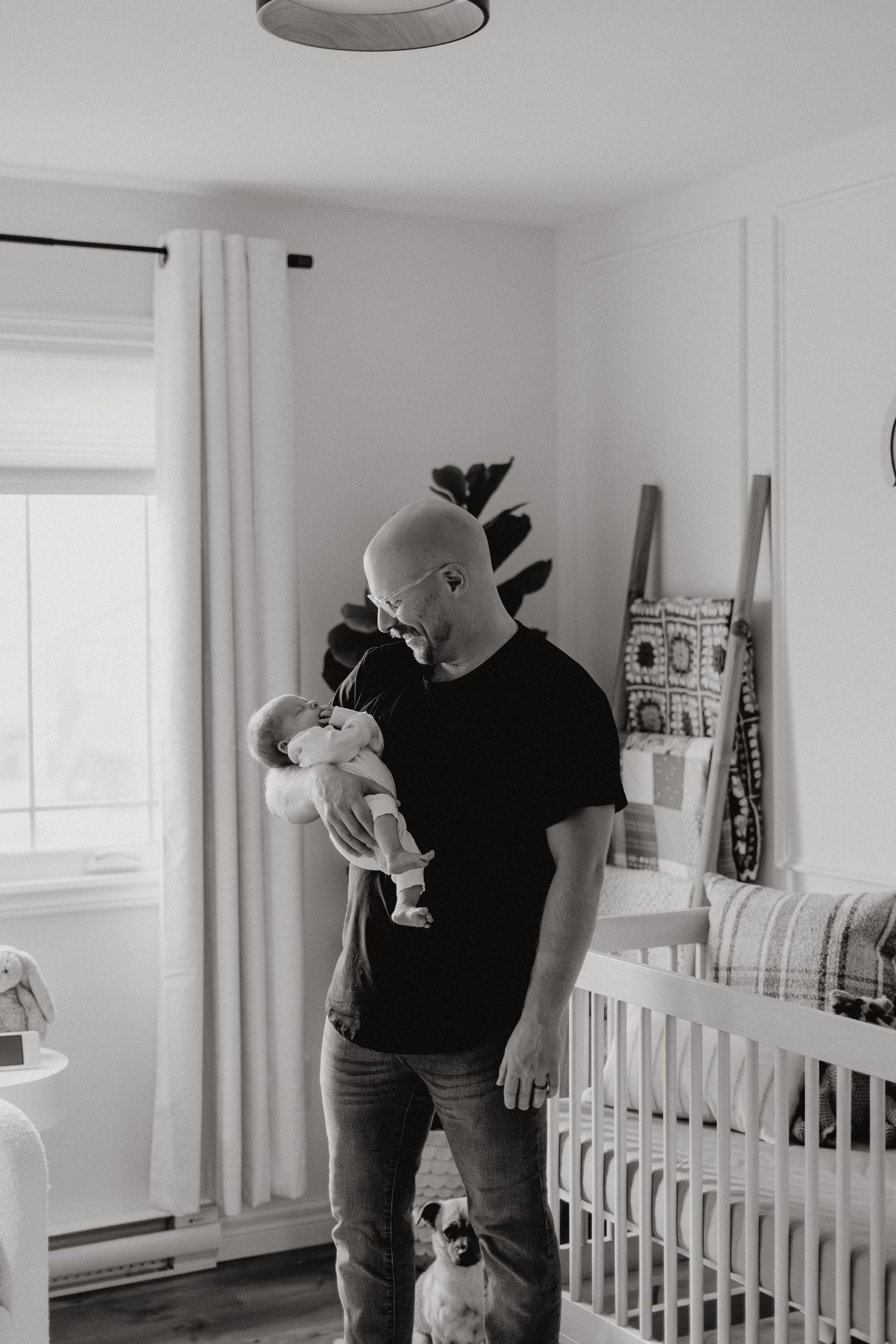 Adult playing with infant near white crib in minimalist nursery setting.