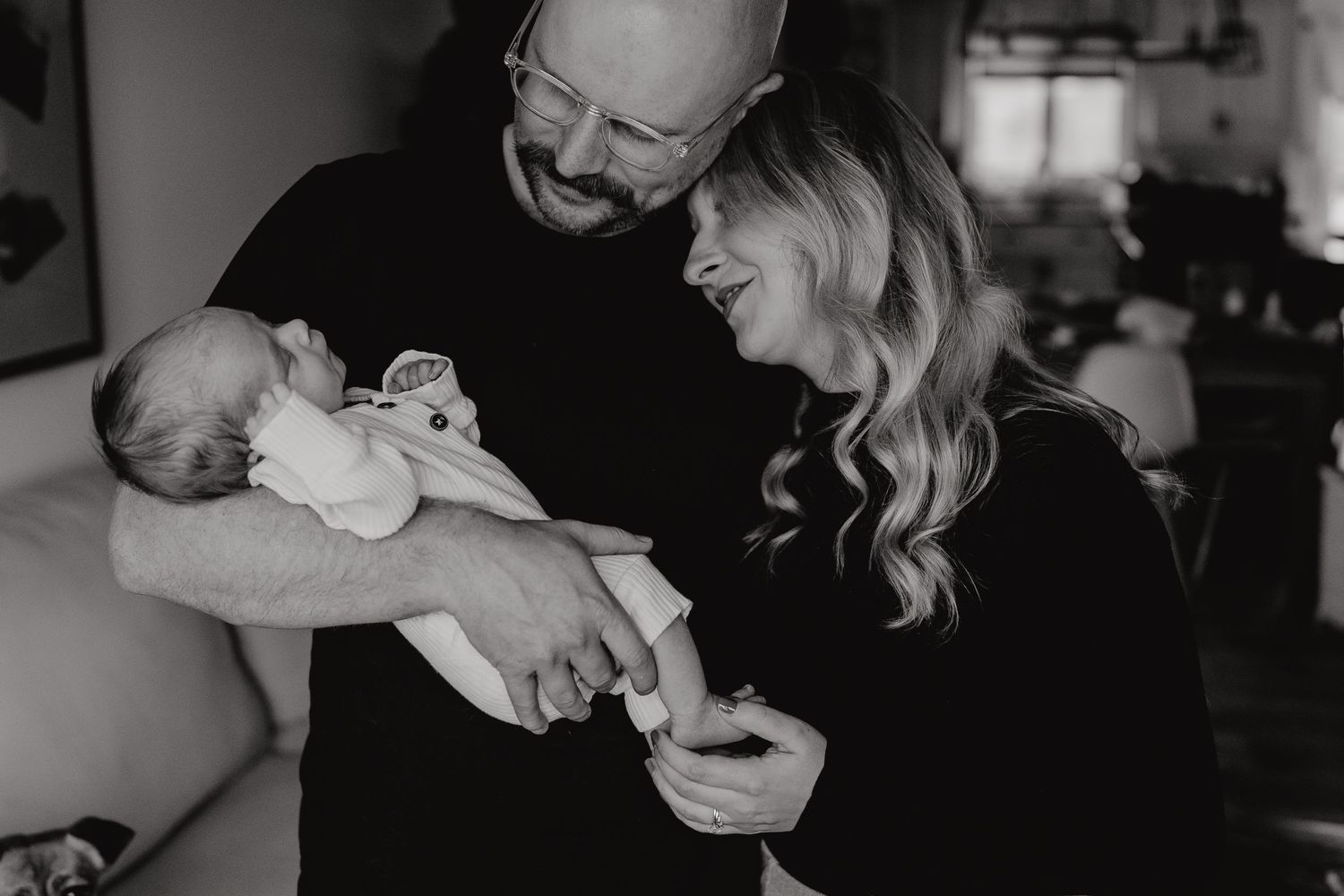 Candid lifestyle photo of parents sharing a laugh while holding their infant.