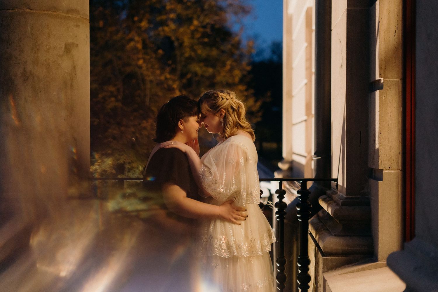 Couple sharing an intimate moment against classic white columns at dusk.