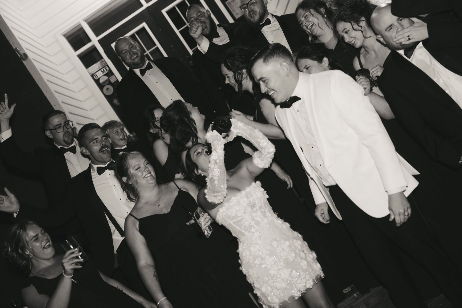 A black and white photo shows a crowded dance floor at a wedding reception with people dancing and celebrating.