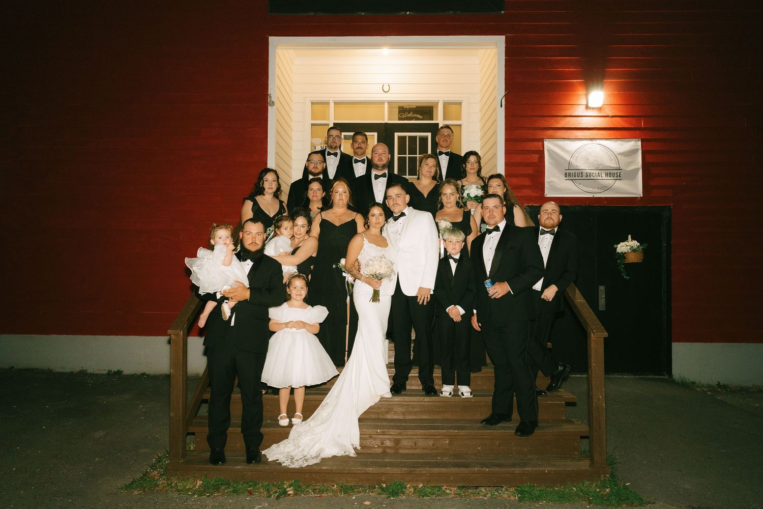 Wedding party poses on wooden steps at dusk with red wall and warm lighting creating an elegant ambiance.