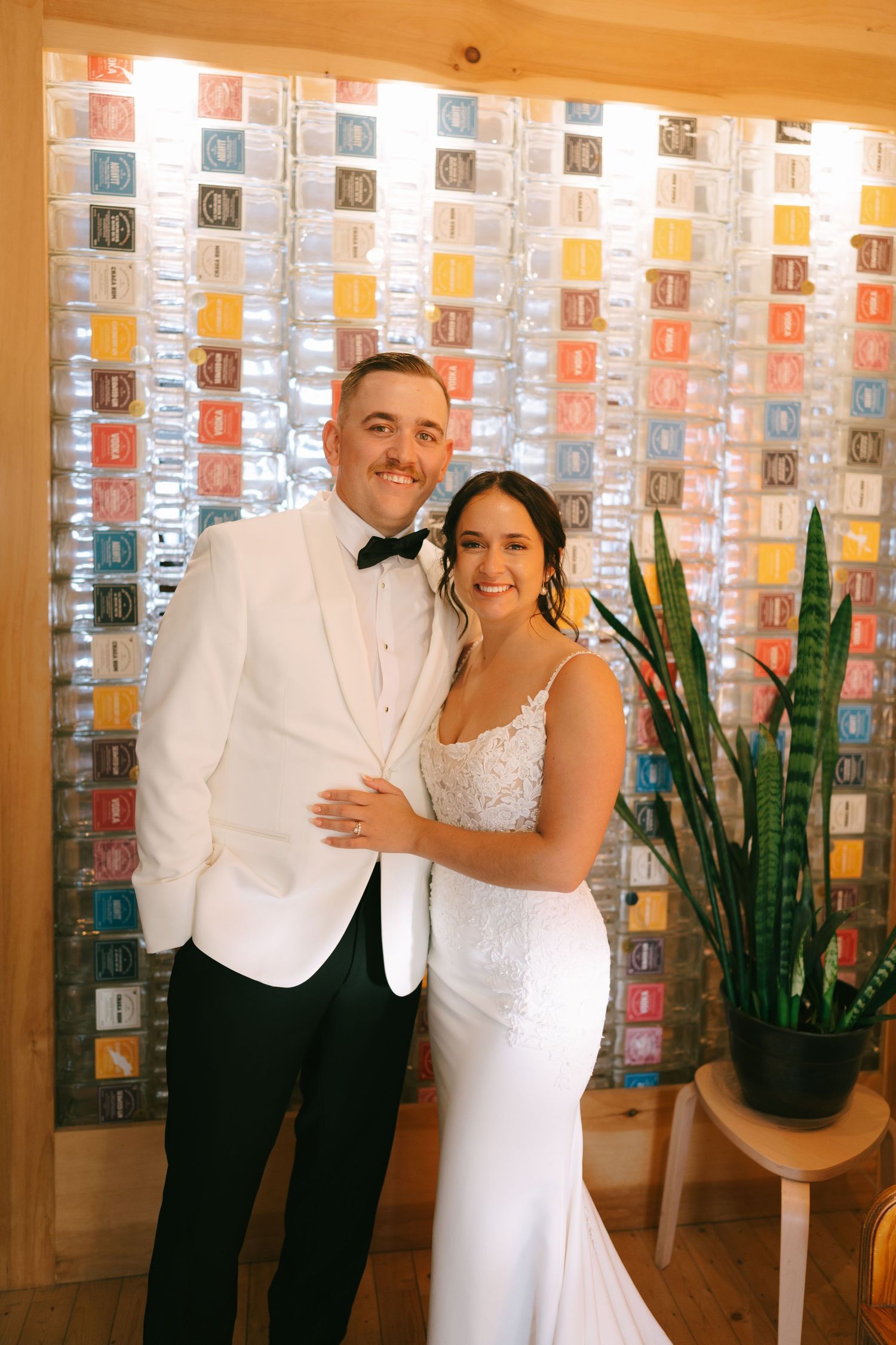 A sequence of three photos showing a couple in white formal attire embracing in front of a decorative wall with plants.