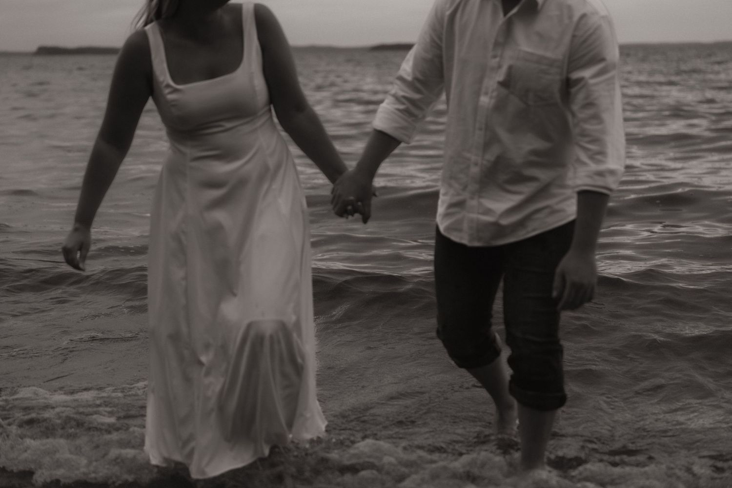Couple walking hand in hand along the beach at sunset in black and white.