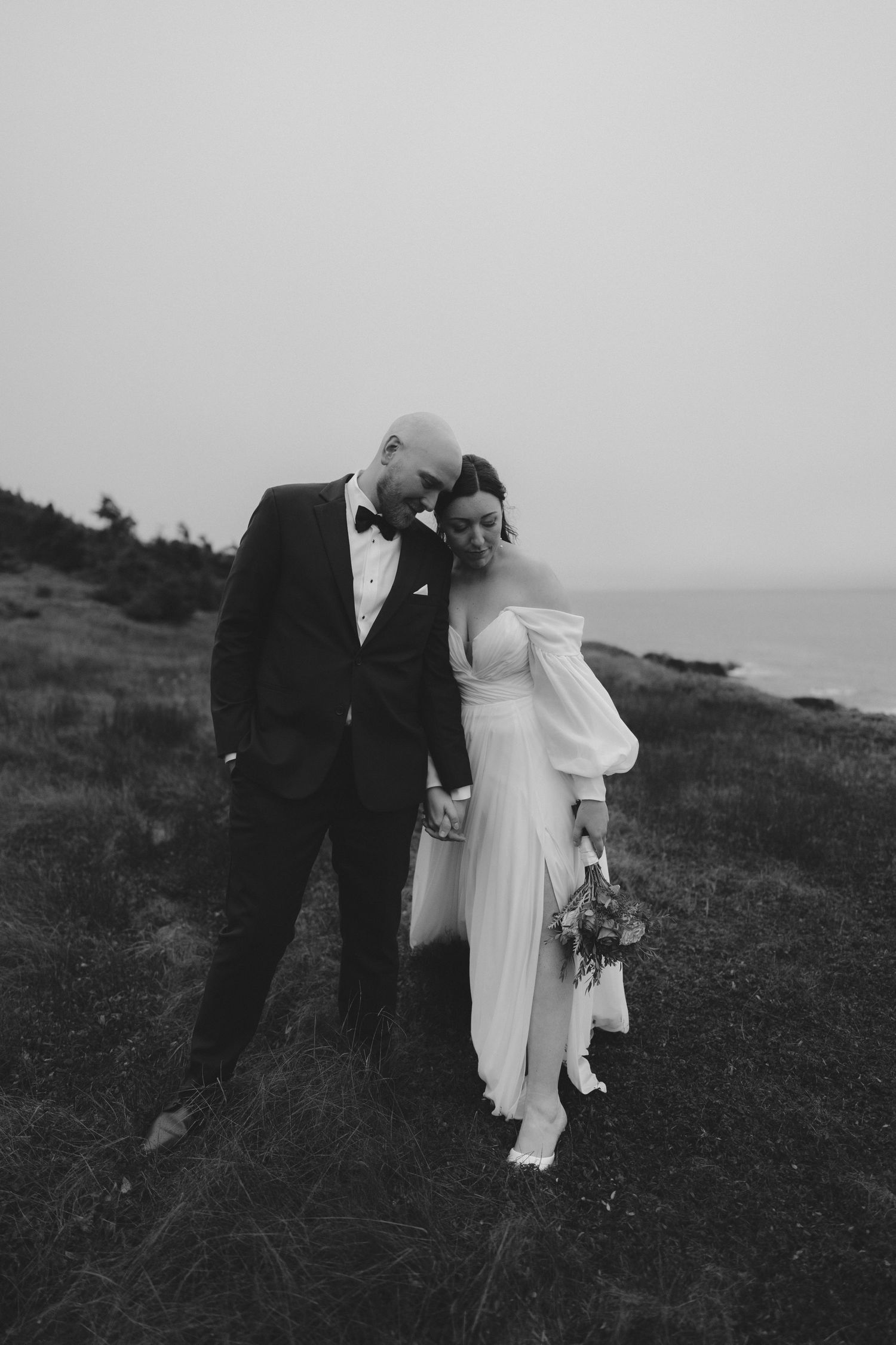 A romantic black and white wedding photo series showing a couple embracing on a coastal hillside.
