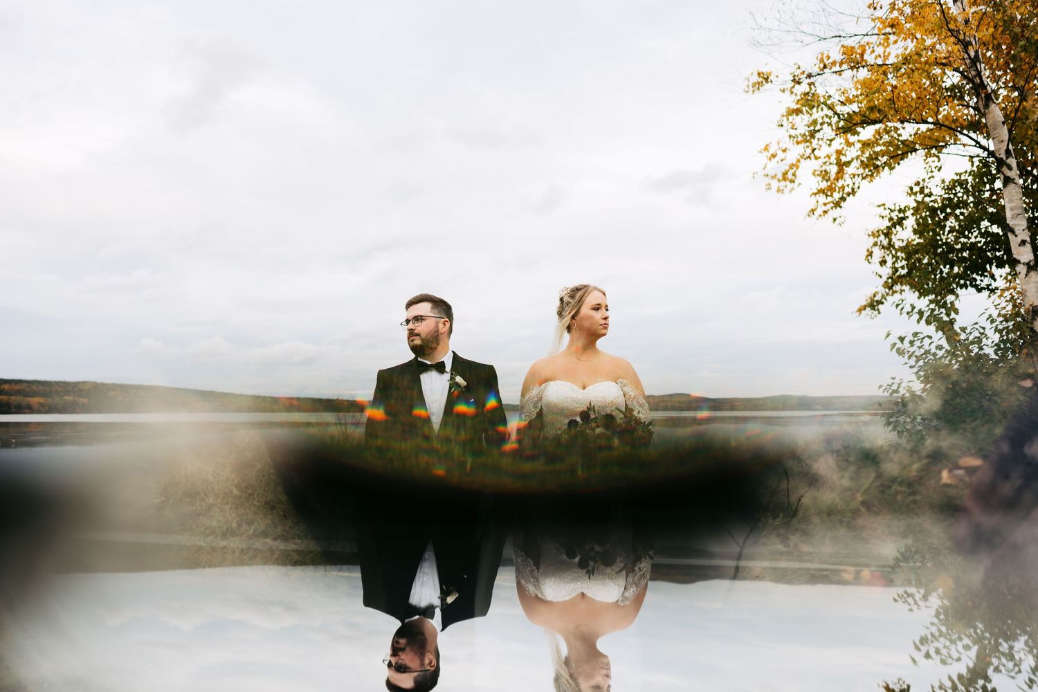A couple stands together at sunset by a lake in autumn, creating a romantic silhouette against the golden sky.
