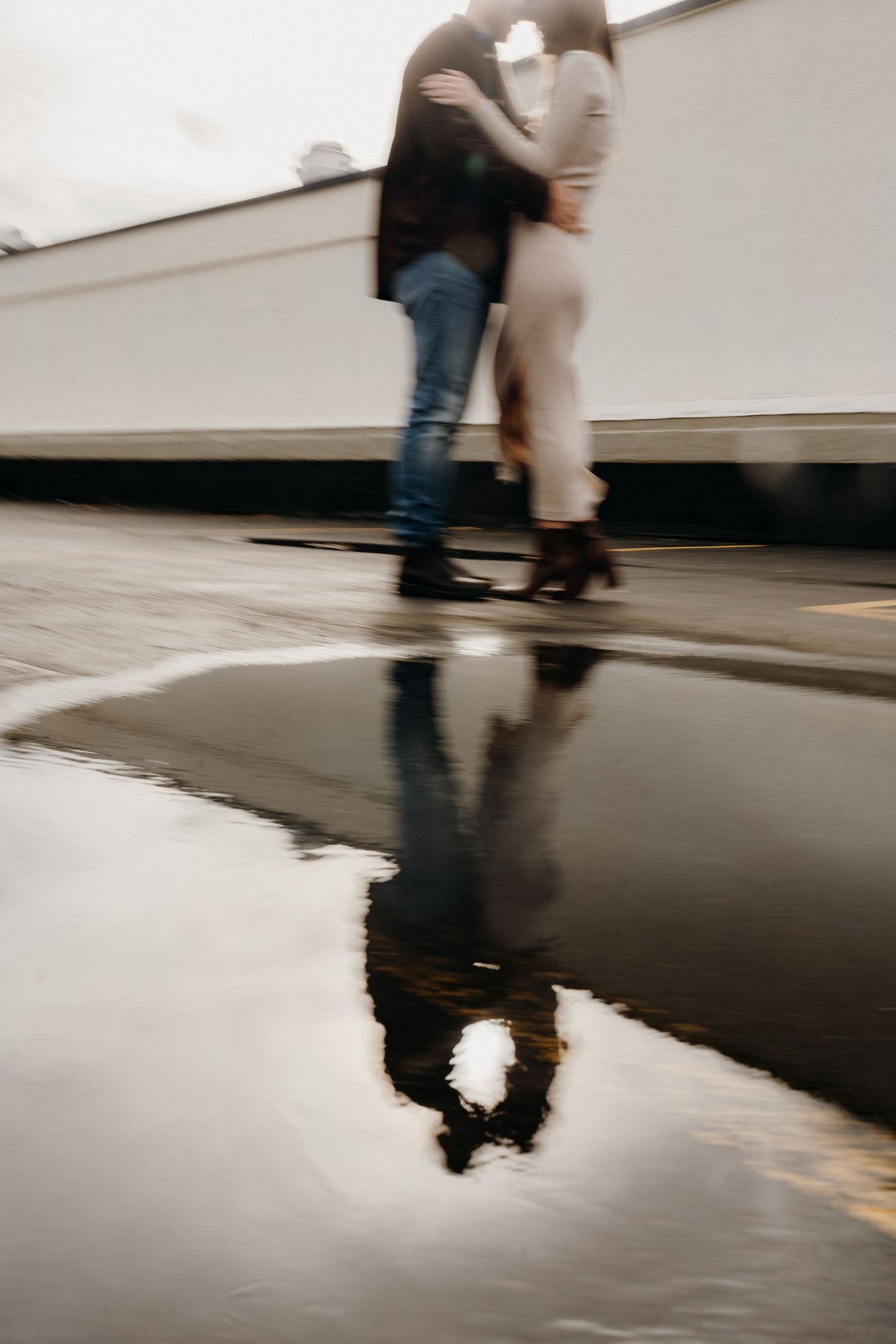 Artistic black and white reflection of two people walking in a wet parking lot surface.
