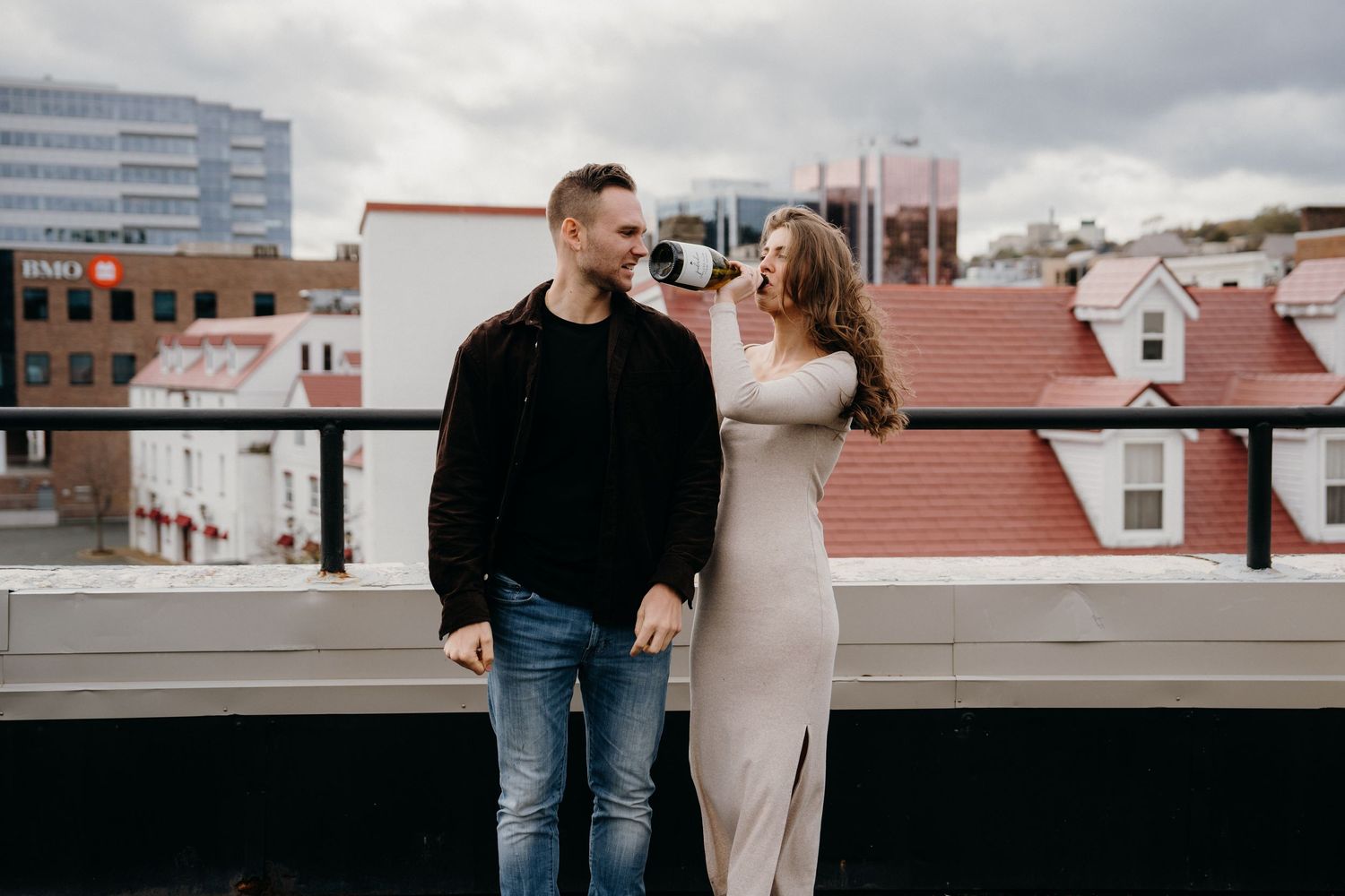 A couple enjoys each other's company while standing on a rooftop overlooking the city.