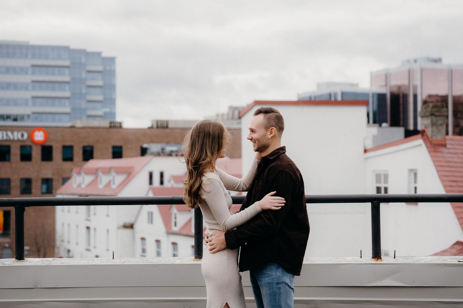 A romantic moment captured between two people on a city rooftop during a cloudy day.