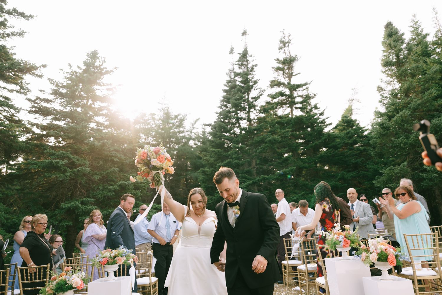 Wedding celebration at an outdoor reception with evergreen trees in the background at sunset.
