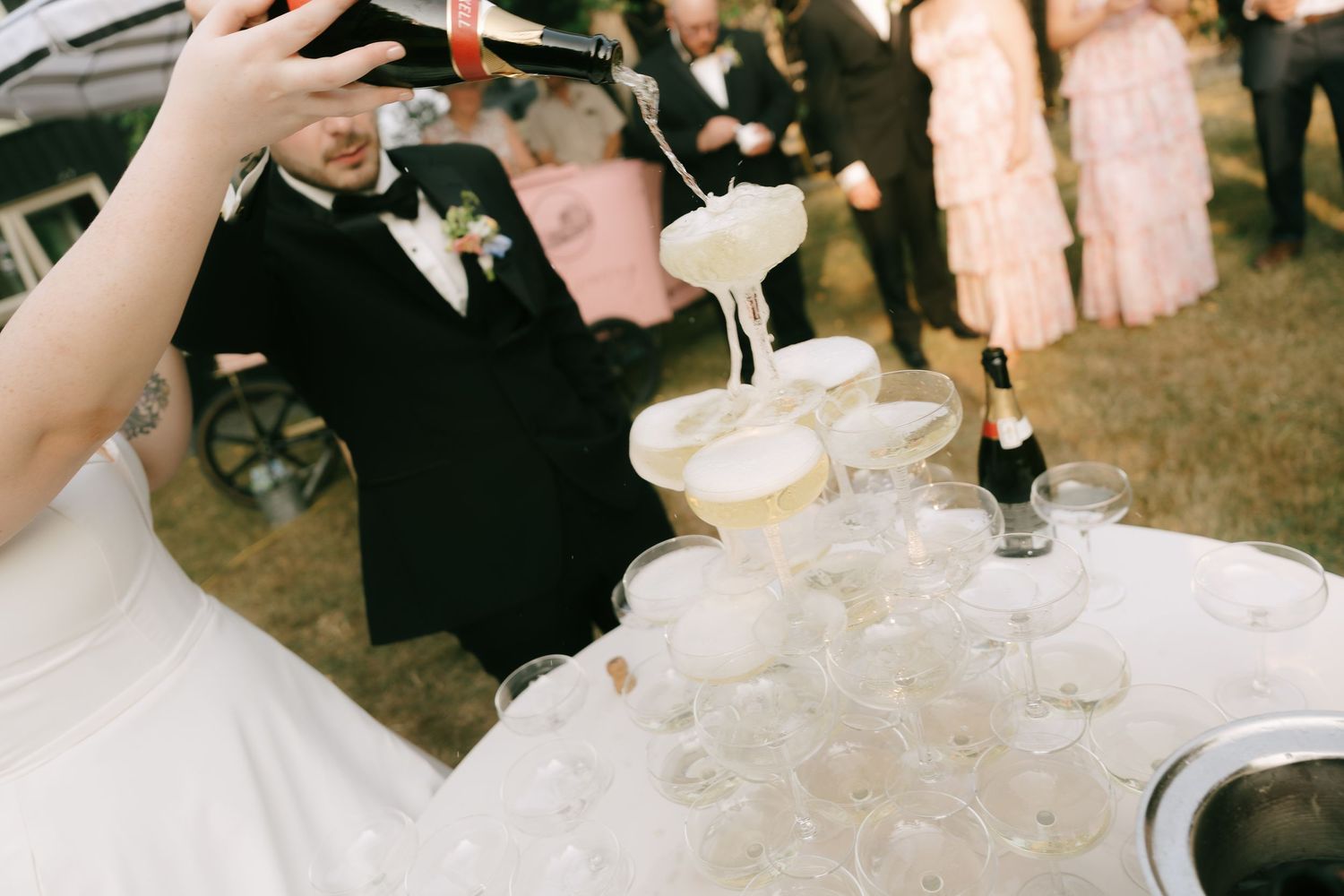 Elegant champagne tower being filled during an outdoor celebration.
