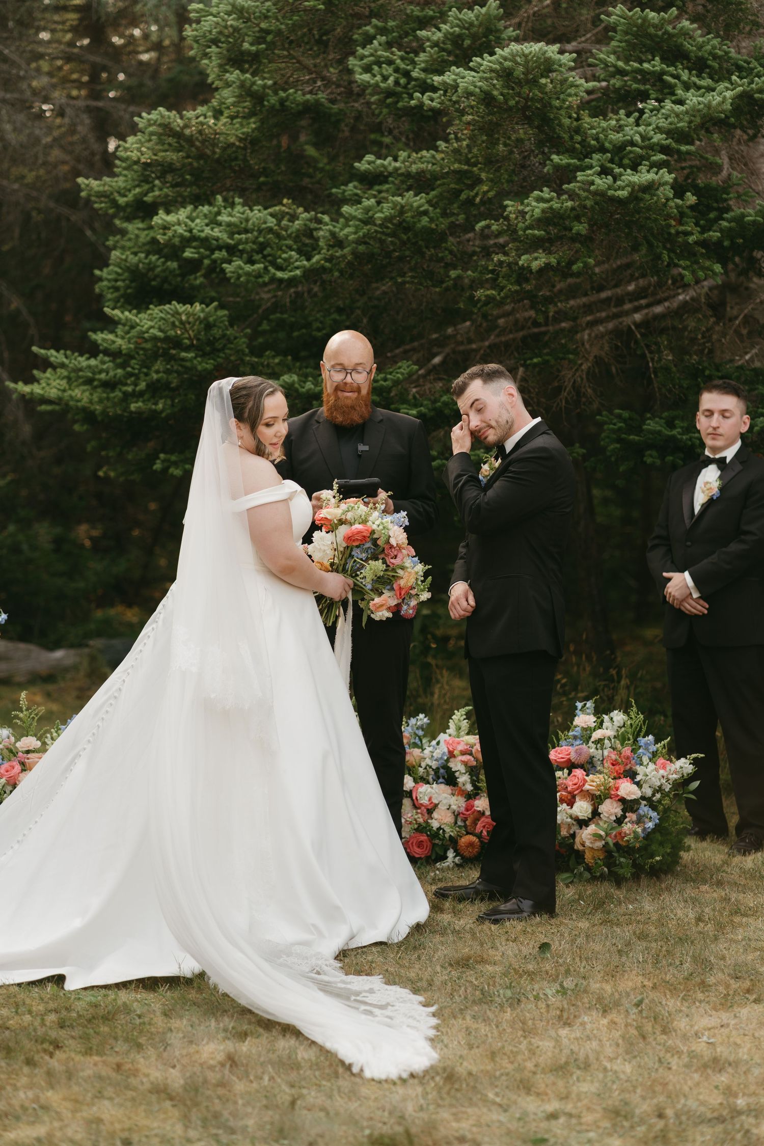Wedding party posing for photos in front of pine trees and floral arrangements.