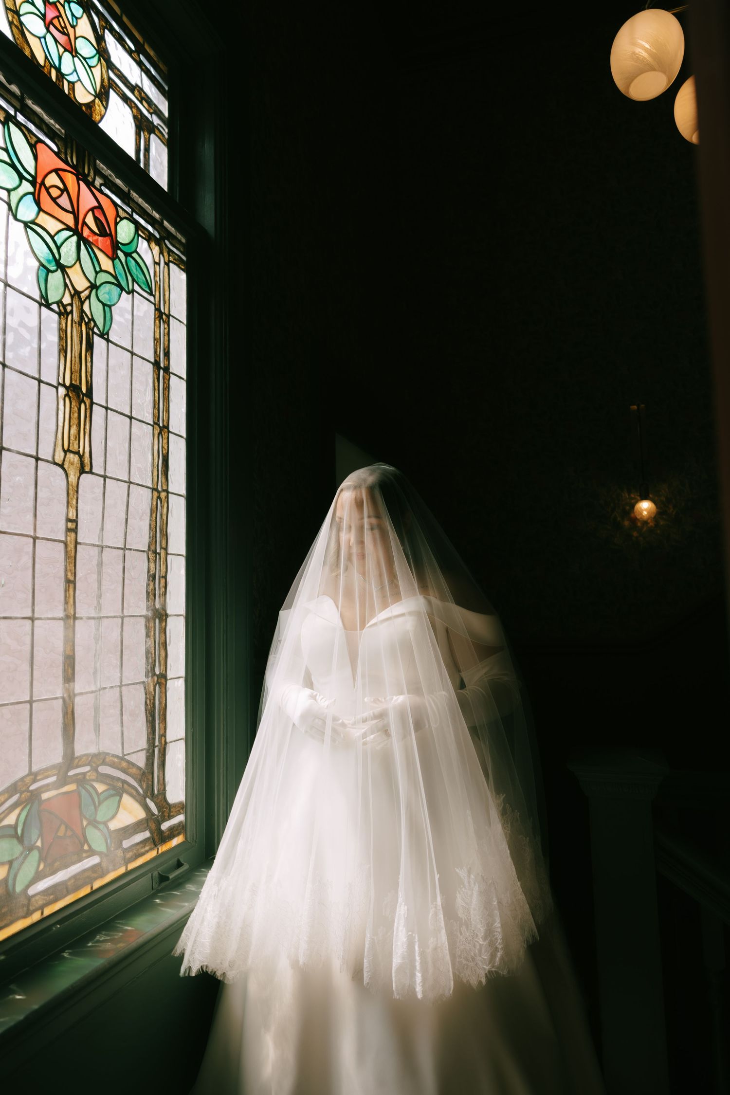Wedding dress silhouetted against ornate stained glass windows with glowing lanterns overhead.