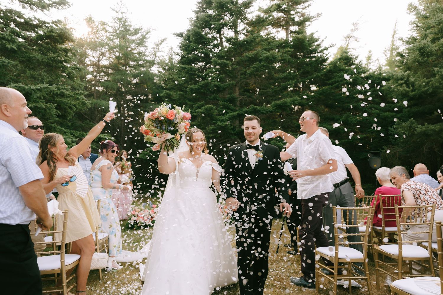 Outdoor wedding celebration with confetti being thrown as guests cheer.