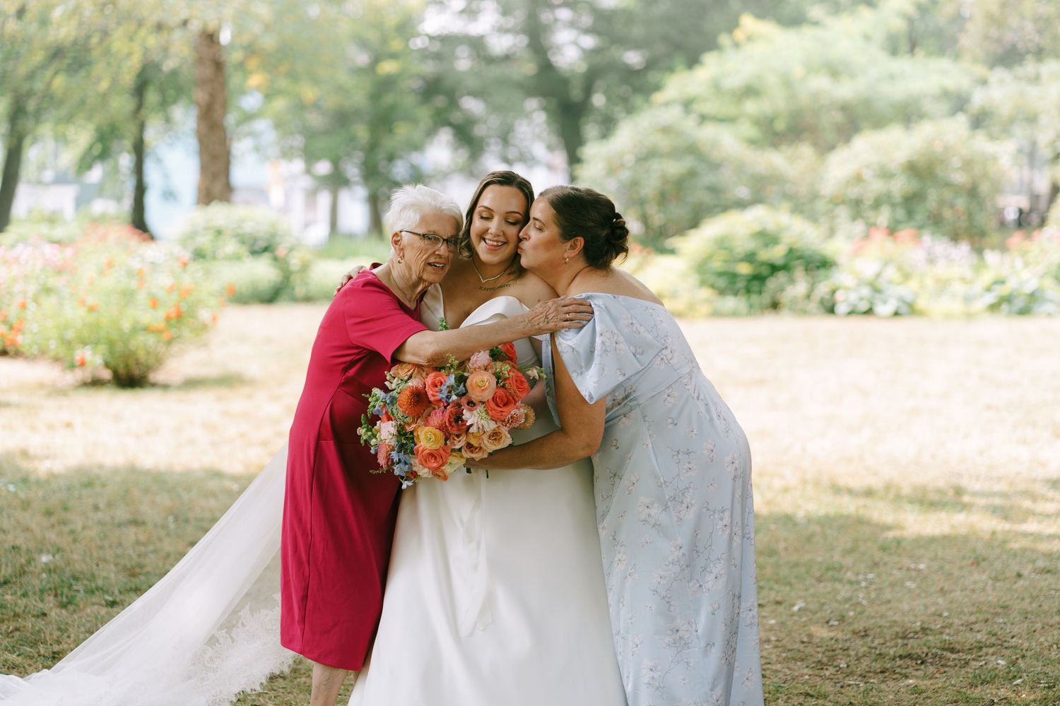 Family members embrace during outdoor wedding photos under shaded trees.