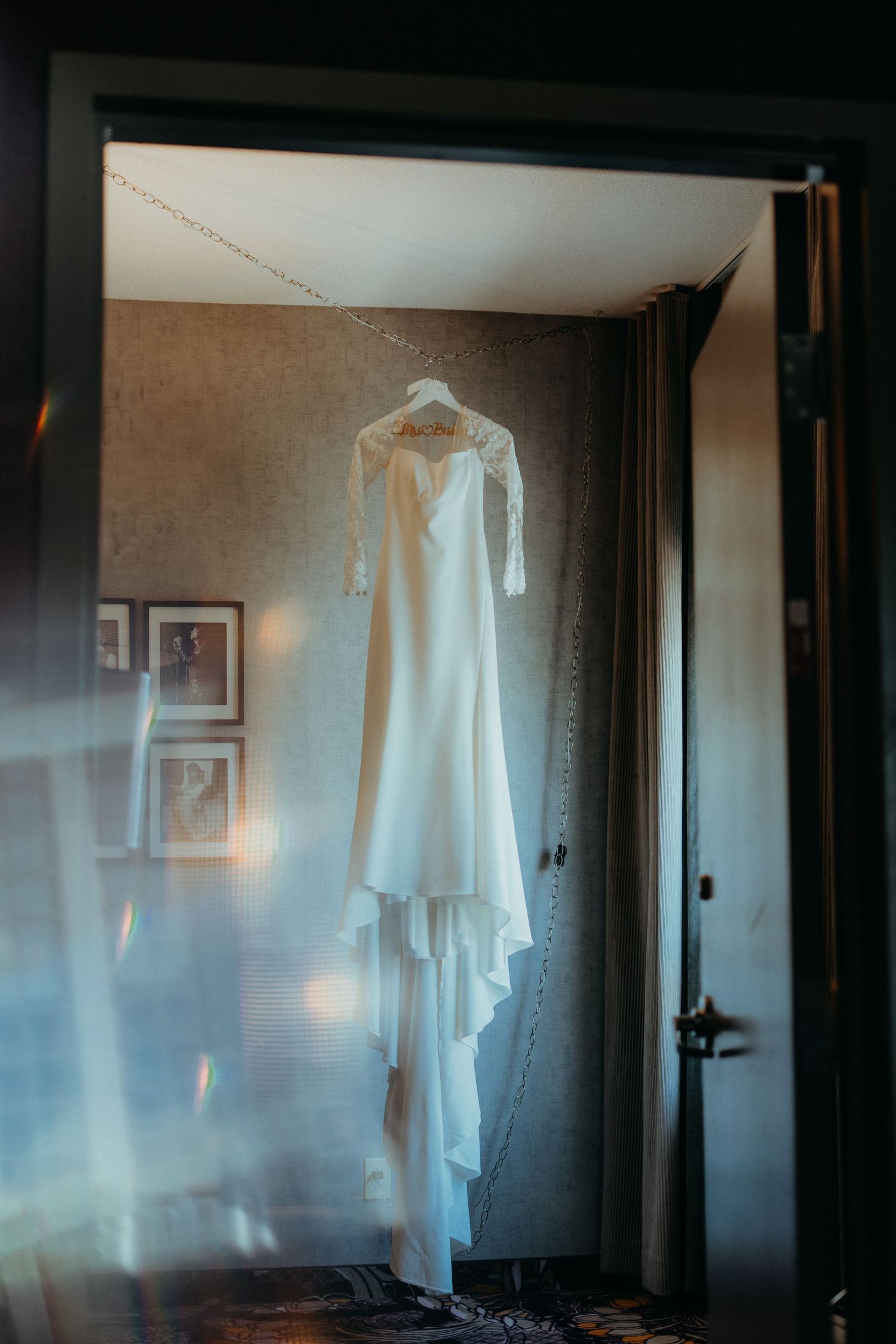 Wedding dress hanging in a sunlit hotel room creating a dreamy silhouette.
