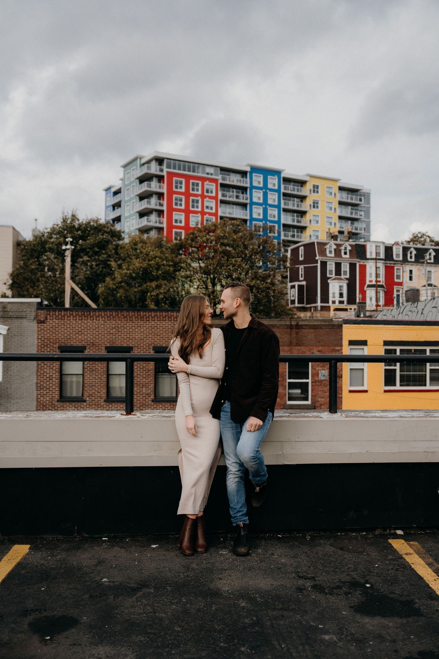 Couple shares intimate moments on urban rooftop with colorful buildings in background.