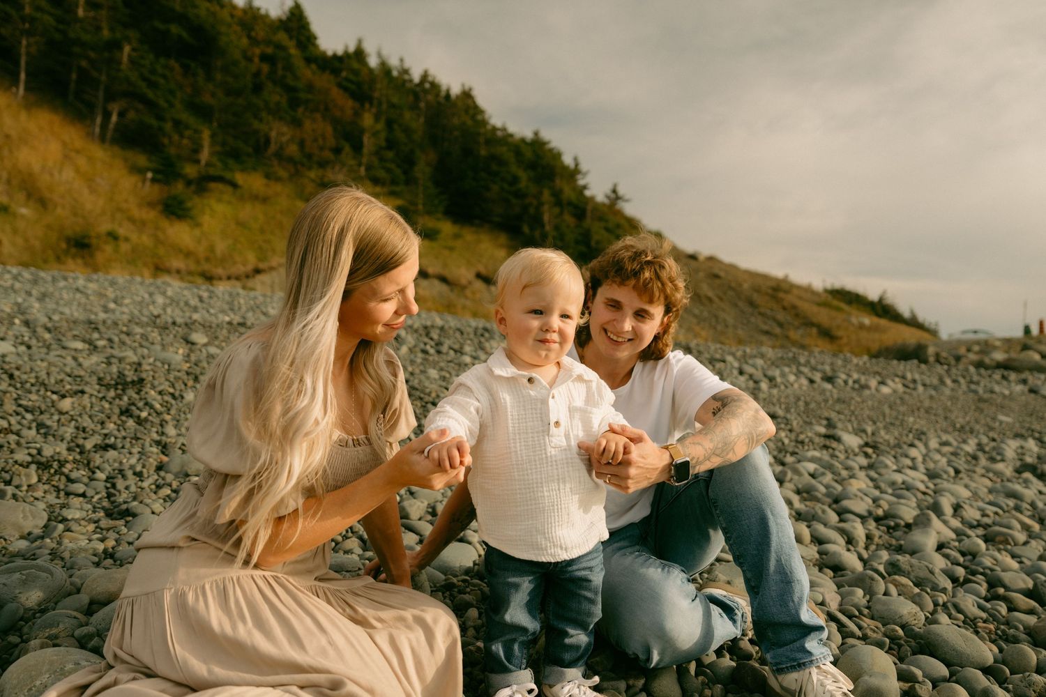 A family sits together on a rocky beach during a cloudy day.