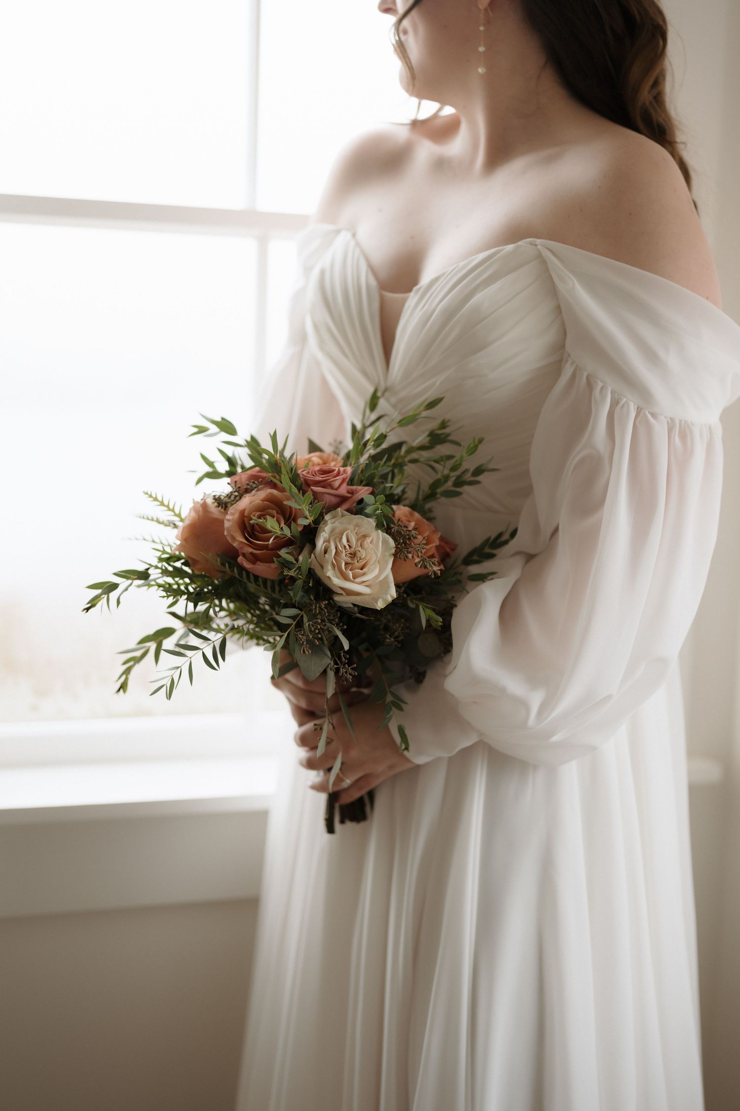A bridal portrait featuring a romantic off-shoulder white gown and pastel floral bouquet.