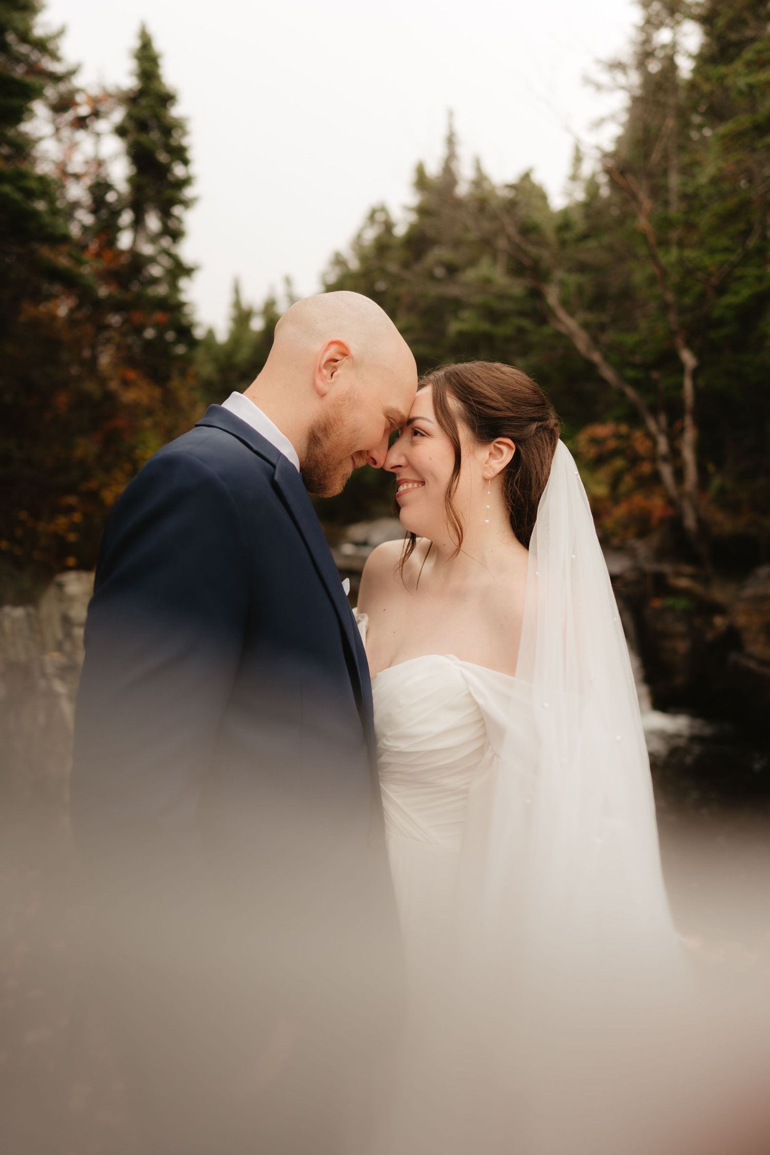 A romantic wedding couple shares an intimate moment in front of evergreen trees during an autumn wedding photoshoot.