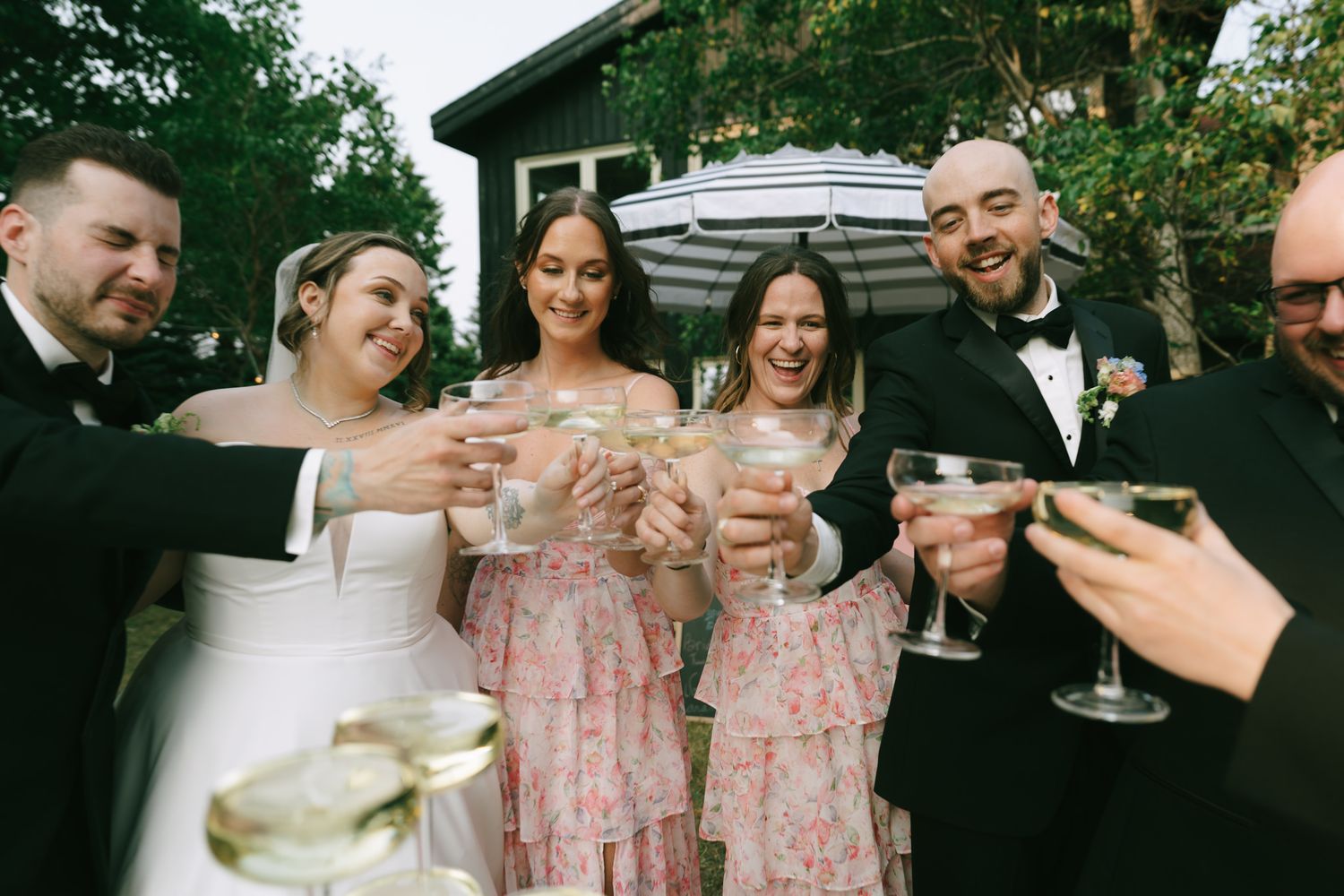 Wedding party celebrates with champagne outdoors under natural lighting.