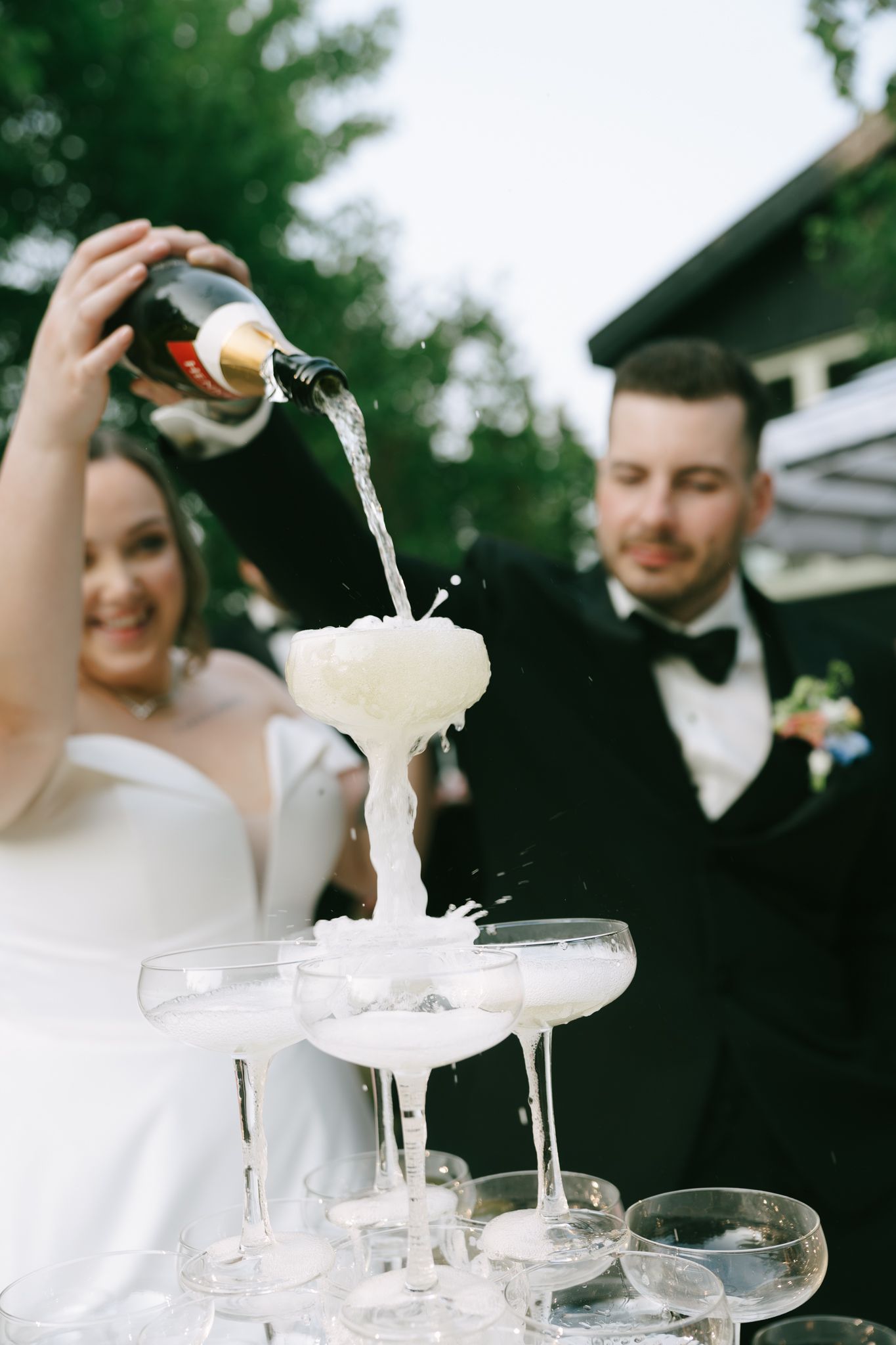 Champagne being poured into a tower of elegant crystal glasses at an outdoor wedding reception.
