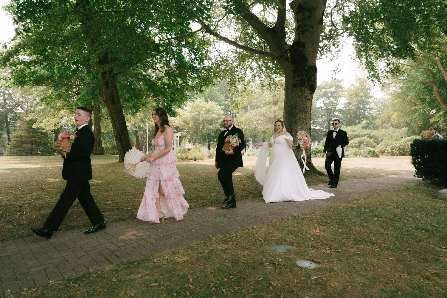 Wedding party walking together under tree canopy in outdoor setting.