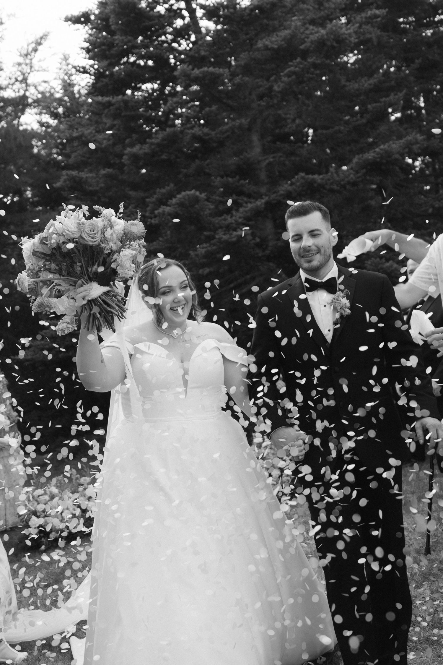 Black and white photo of a joyous wedding celebration with confetti flying through the air.