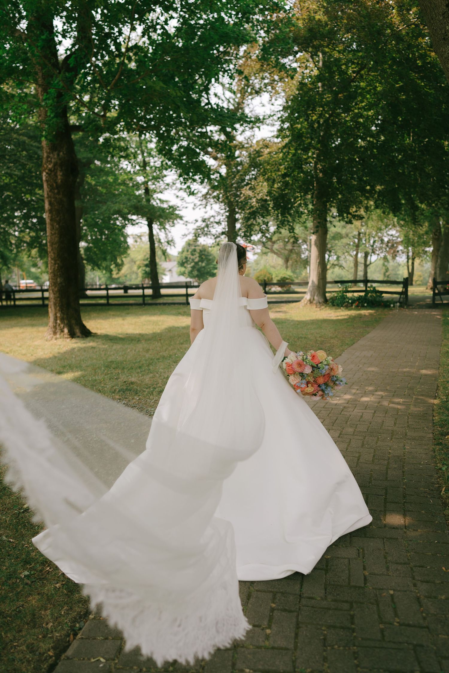 Wedding dress with flowing train captured in dynamic movement across a brick pathway outdoors.