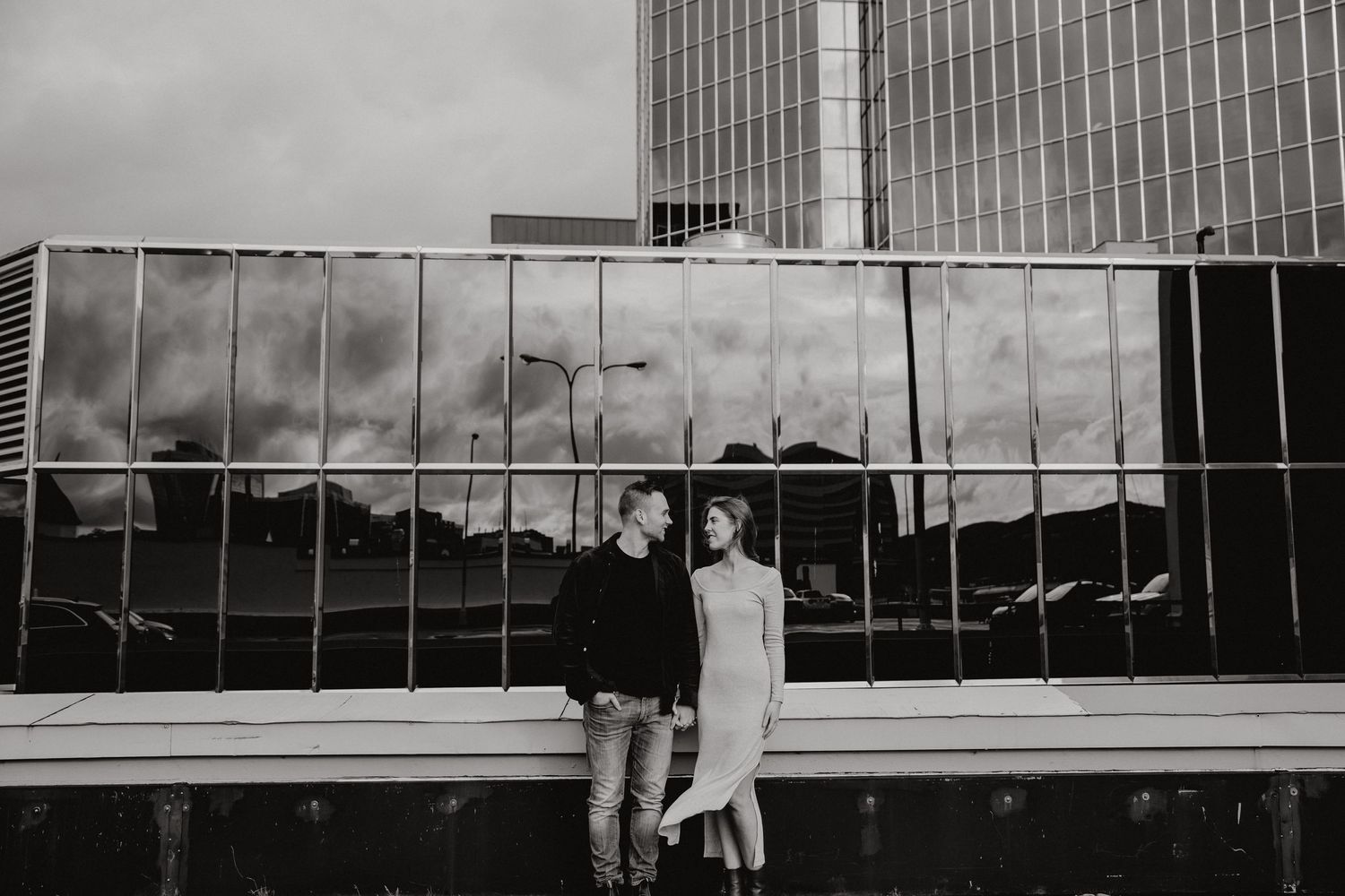 A couple shares a tender moment on a rooftop with dramatic cloudy skies in the background.