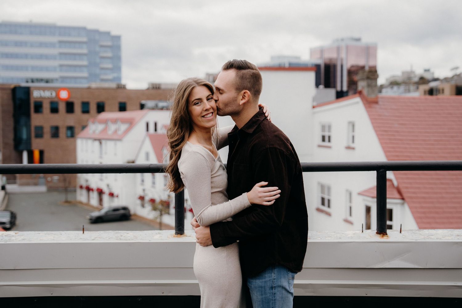 A tender moment between two people on a rooftop with red-roofed buildings in the background.