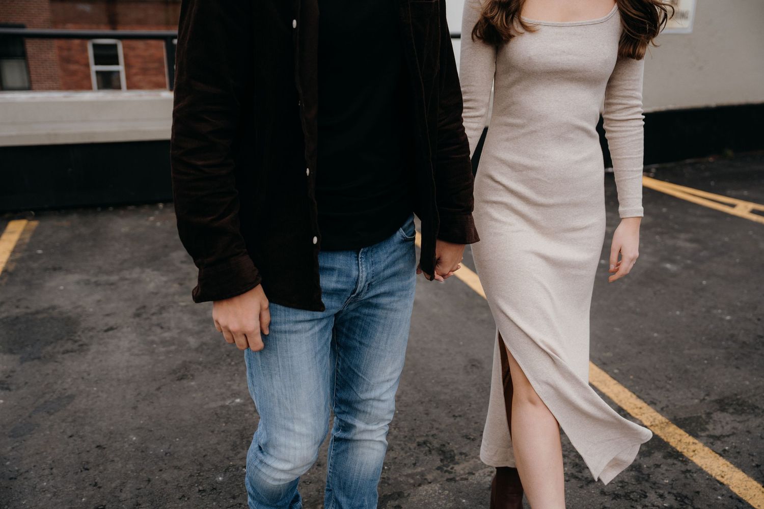 A couple stands close together in front of industrial brick buildings.