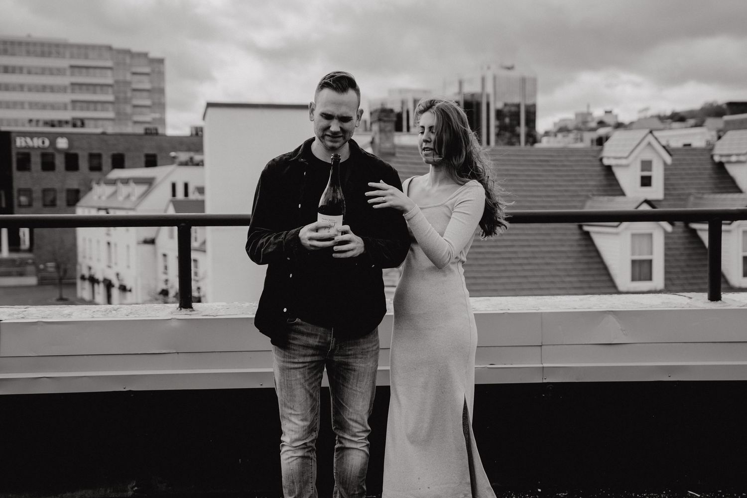 A couple shares laughter on a rooftop deck with city buildings in the background.