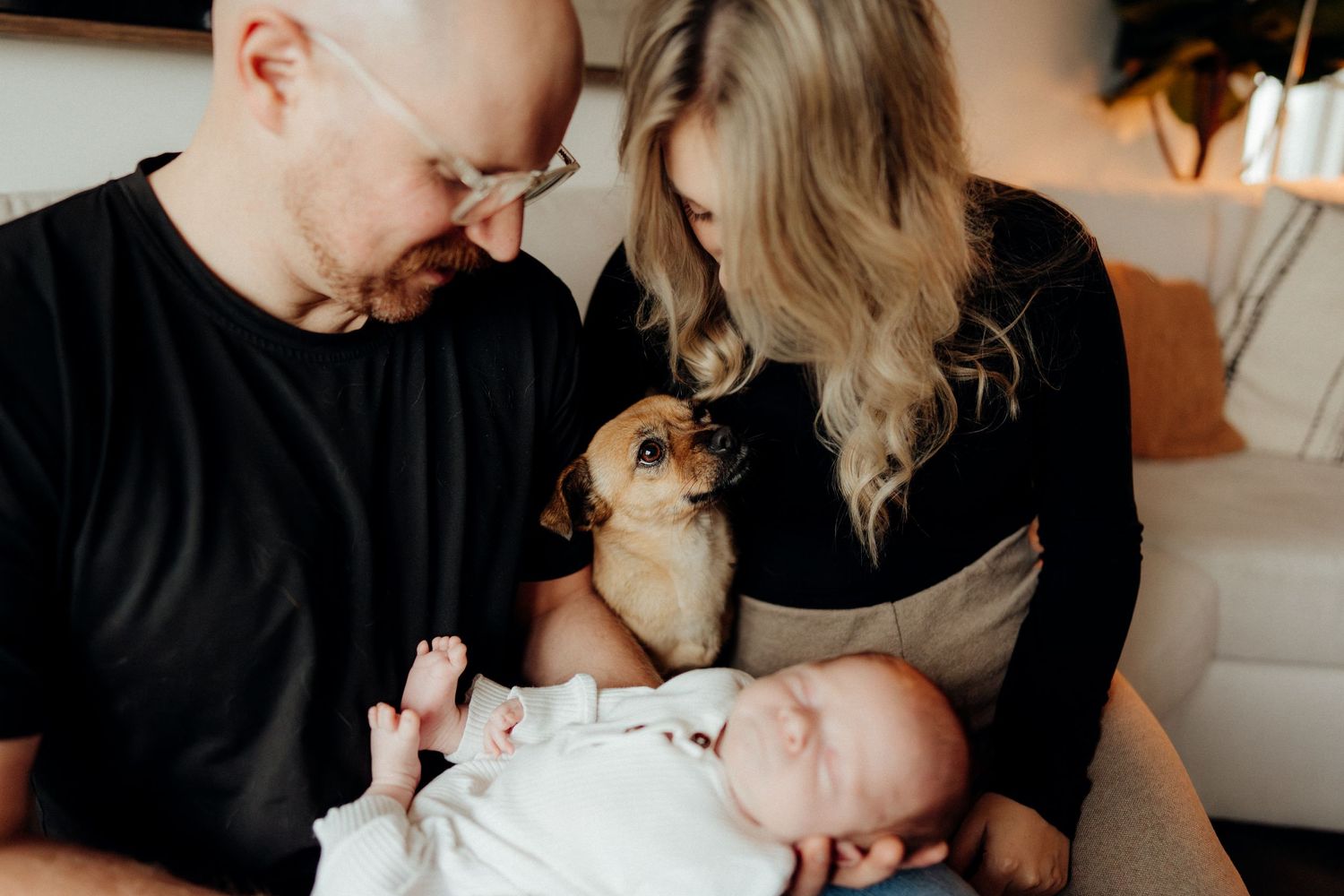 Parents share a tender moment with their newborn while their curious dog peeks between them.