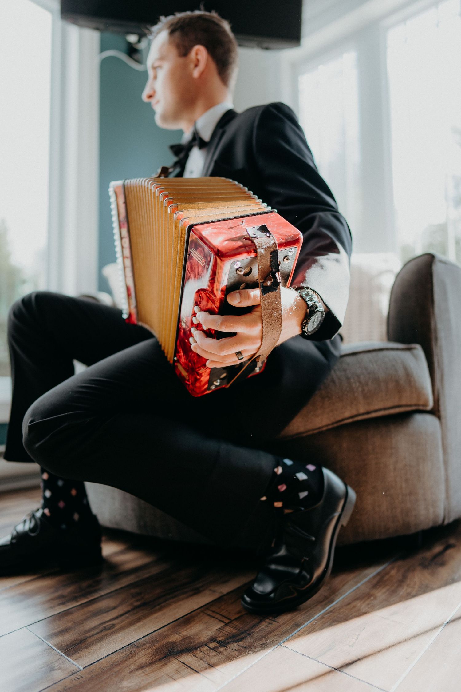 Multiple angles of musician playing red accordion on brown couch in sunlit room.